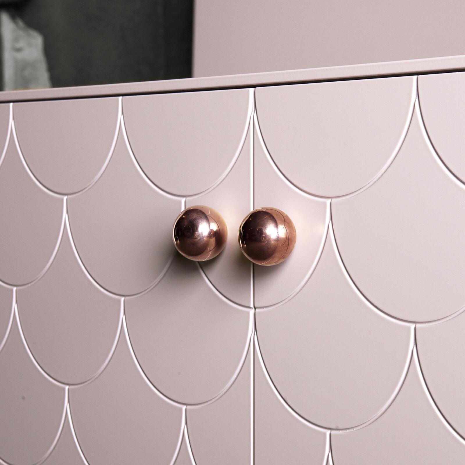 Handtag i koppar på rosa sideboard med mönster som liknar fiskfjäll