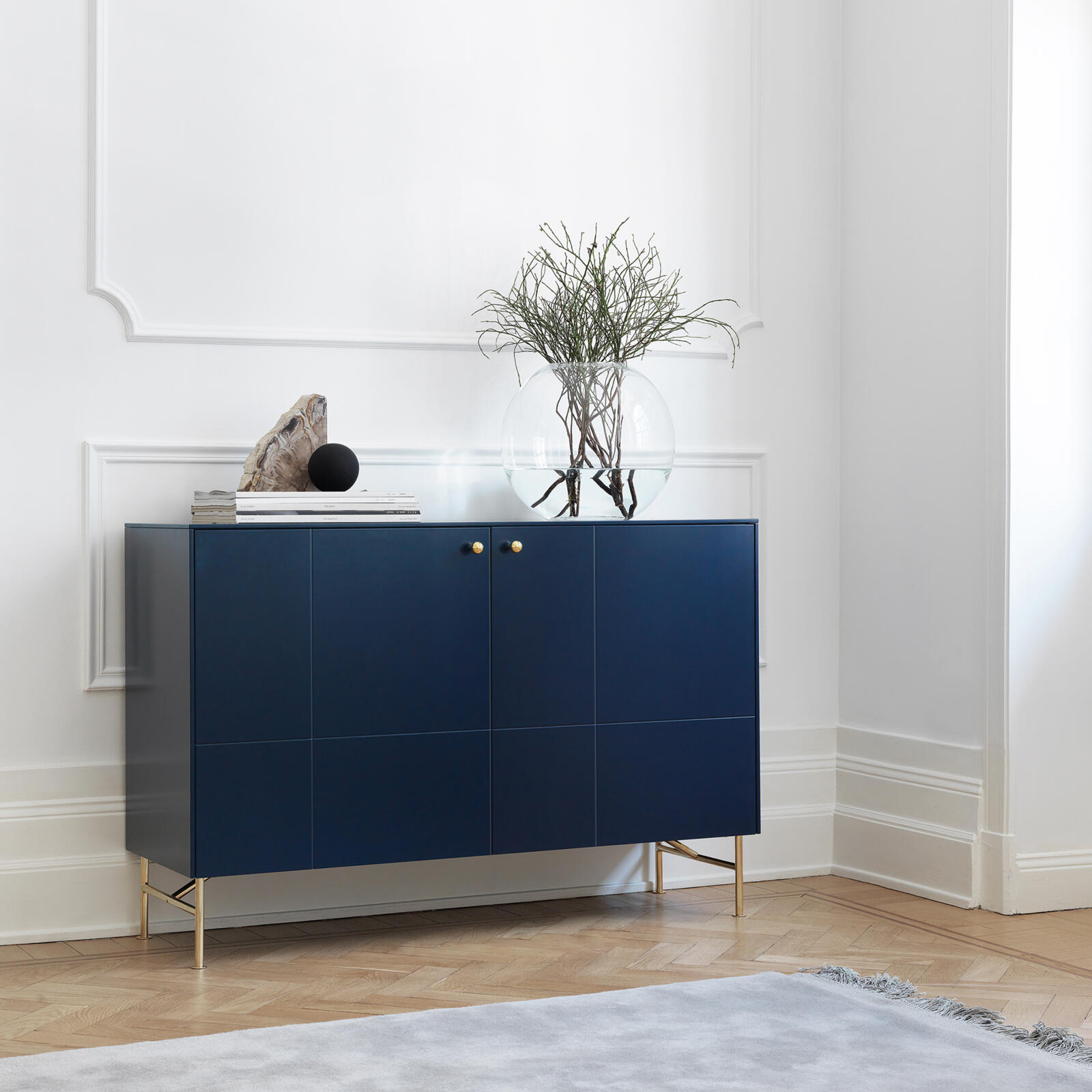 Dark blue sideboard in a living room, with handles and legs in brass